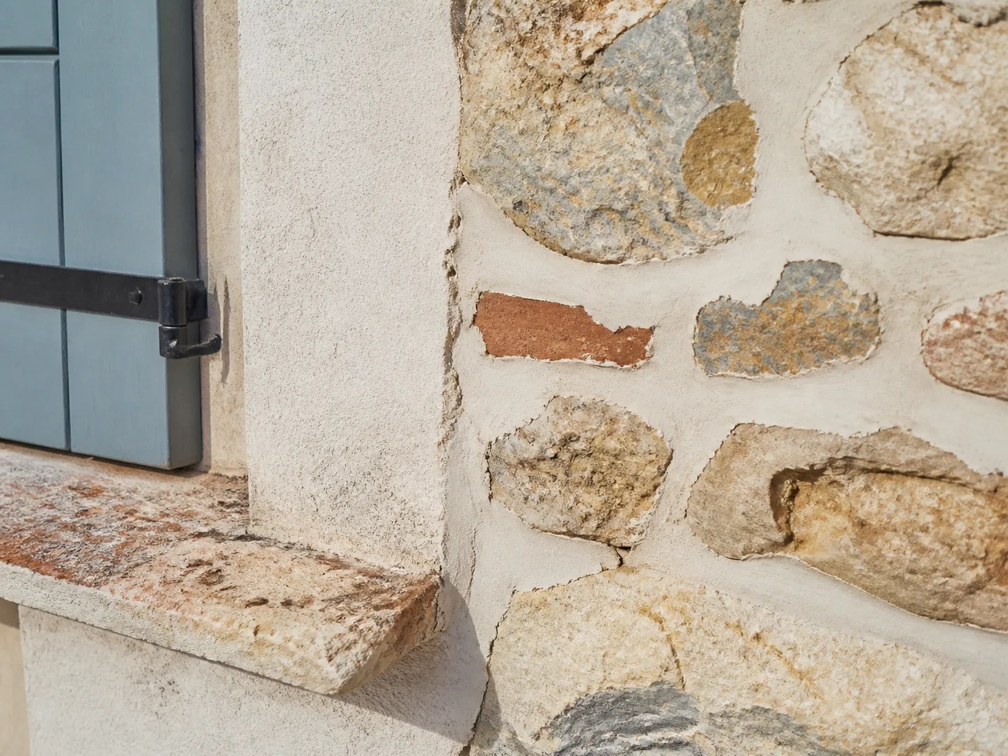 Un jardin de gravier clair devant une maison basse à toit de tuiles, un arrosoir posé près d’un massif de graminées, lumière de fin d’après-midi, cadrage large.