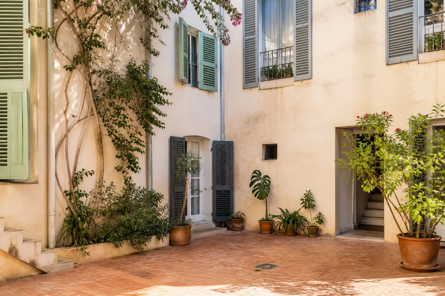Cour méditerranéenne aux murs enduits, volets et sol en terre cuite